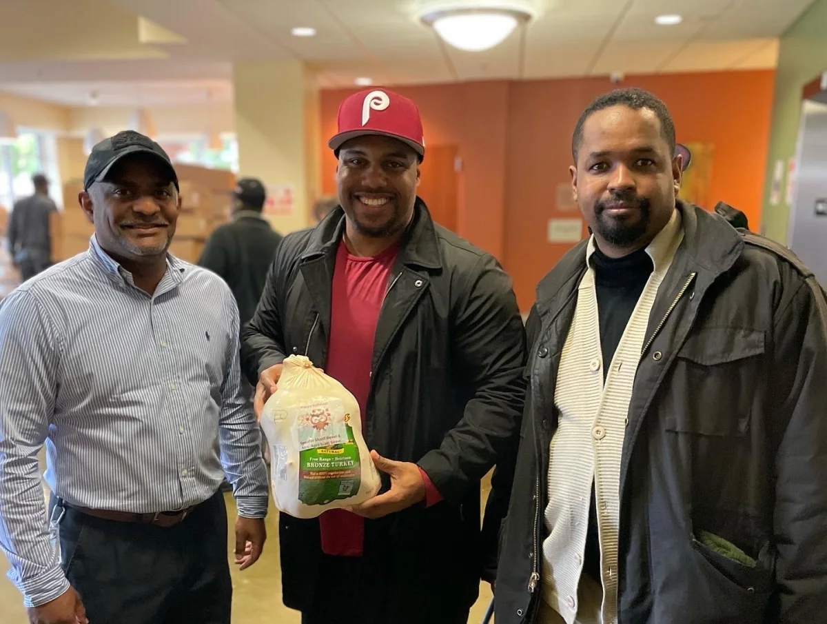Three men smiling, holding a turkey labelled with a custom Happy Holidays label